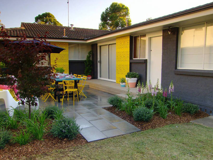 Bold Yellow Feature Wall in Backyard with Black Painted Brick and Tiled Pathway and garden and porch